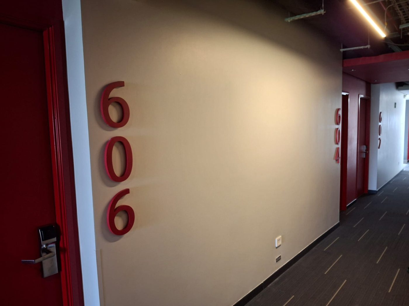 Números 606 fabricados como letras 3D dimensionales en color rojo mate instaladas como señalización corporativa en pasillo de hotel u oficinas en Monterrey por Punto Clave