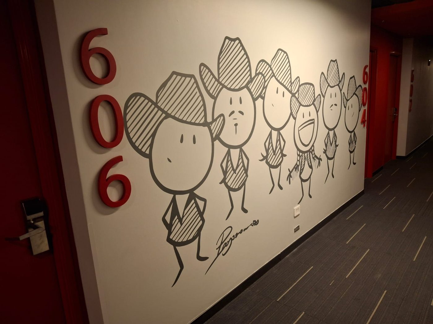 Mural decorativo ilustrado con personajes vaqueros en vinil de corte gris sobre pared blanca instalado por Punto Clave en pasillo corporativo de Monterrey