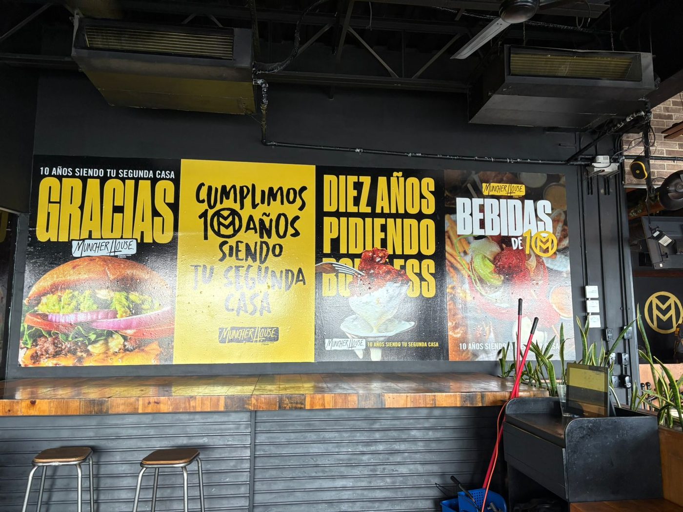 Mural impreso de gran formato celebrando 10 años de aniversario del restaurante Muncher House con 4 paneles tipográficos sobre productos del menú instalado por Punto Clave