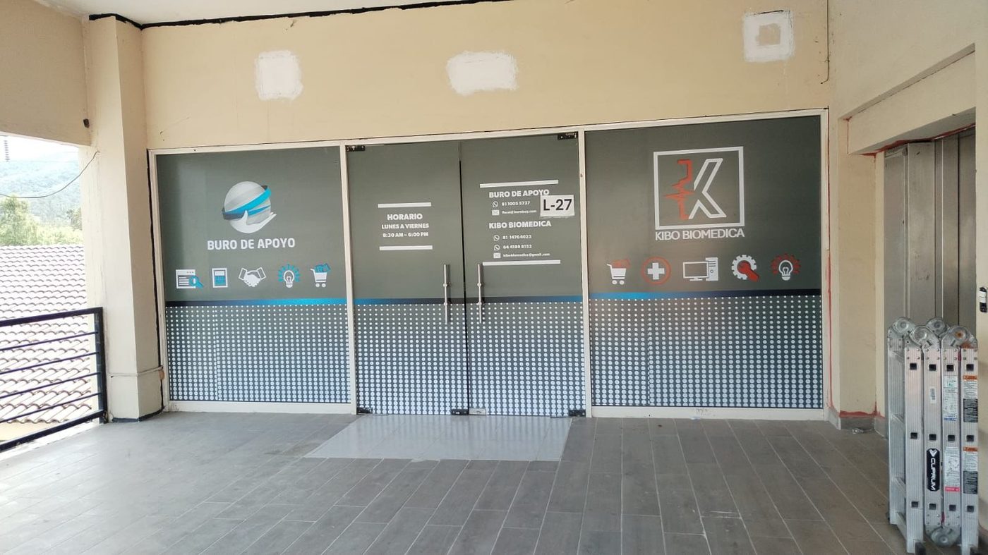 Frente de oficinas con rotulación impresa de Buro de Apoyo y Kibo Biomédica incluyendo logos, horarios, datos de contacto y banda de privacidad instalada por Punto Clave