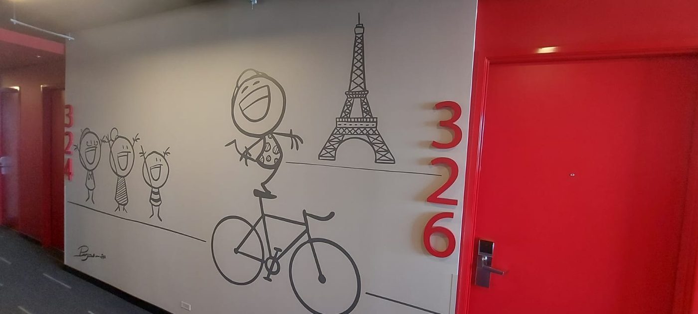 Mural vinílico ilustrado con personaje en bicicleta y Torre Eiffel acompañado de letras 3D de los números 326 en rojo, instalado en pasillo de hotel temático por Punto Clave en Monterrey