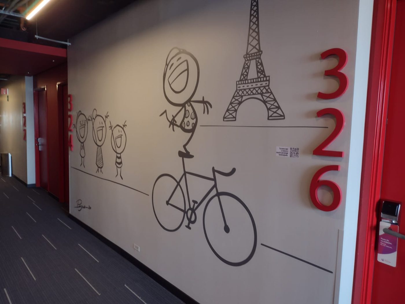 Vista alternativa del mural temático París con personaje en bicicleta junto a la Torre Eiffel y letras 3D de números 326 en pasillo de hotel instalado por Punto Clave