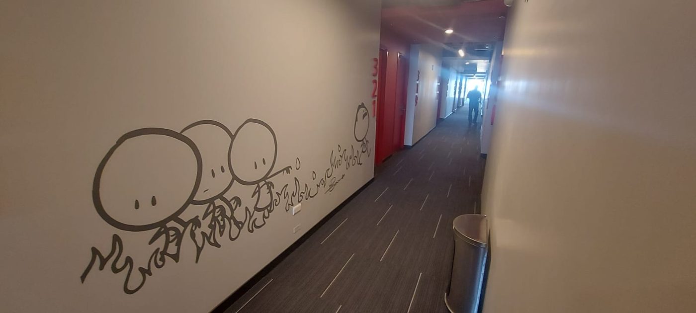 Vista panorámica de pasillo de hotel mostrando mural ilustrado con personajes en perspectiva, puertas rojas, y letras 3D de números de suite, instalado por Punto Clave en Monterrey