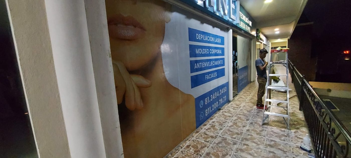 Instalación en proceso de vinil impreso gran formato en fachada de clínica de tecnología láser con técnico de Punto Clave trabajando con escalera en Monterrey