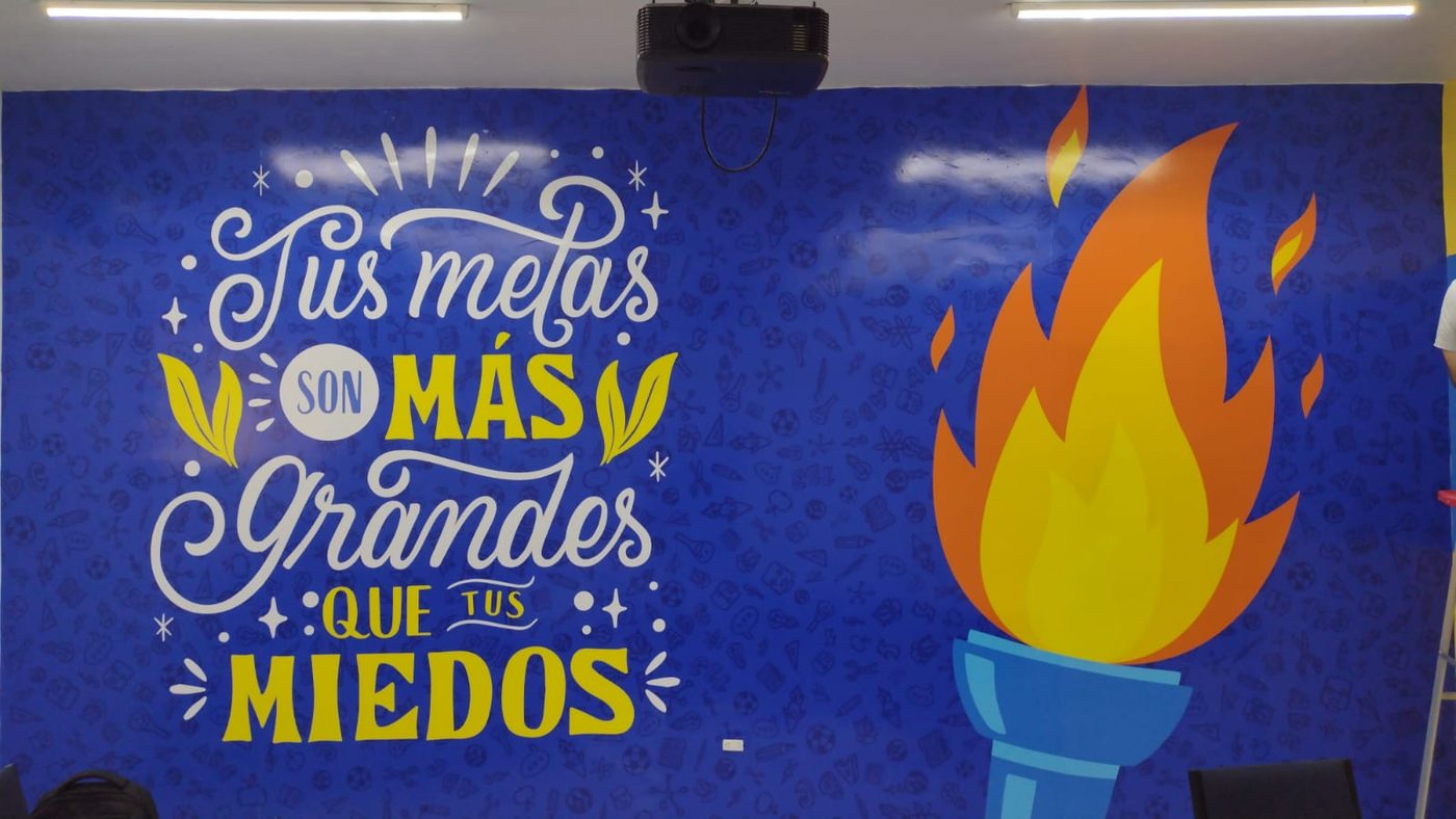 Mural escolar motivacional con frase 'Tus metas son más grandes que tus miedos' en tipografía caligráfica sobre fondo azul con antorcha encendida ilustrada, instalado por Punto Clave