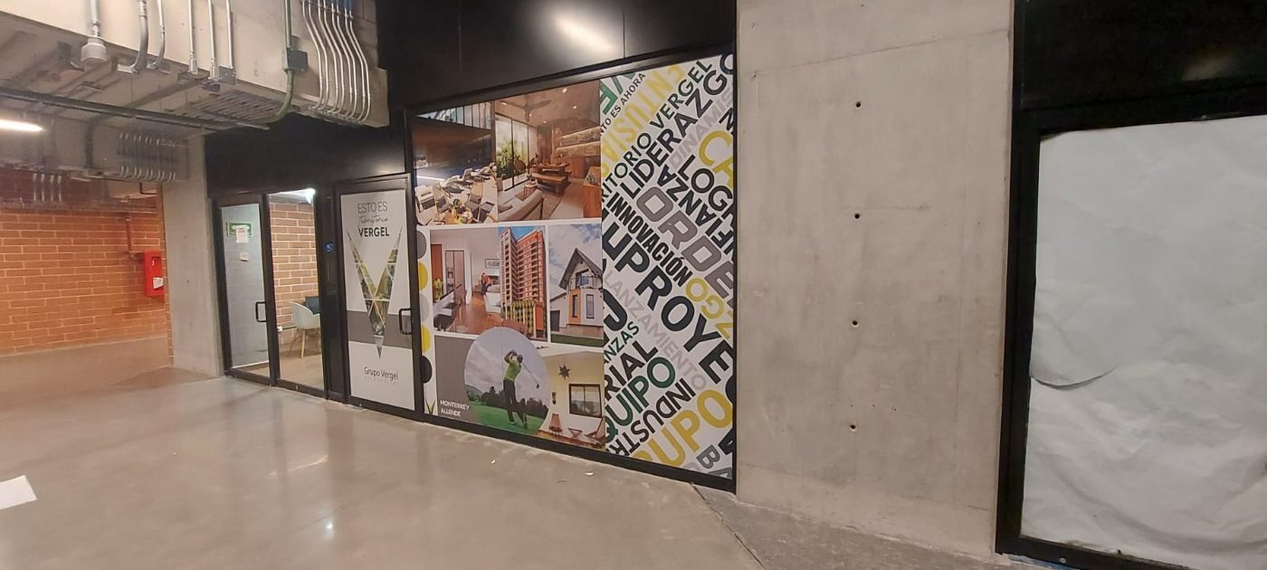 Lobby corporativo de Grupo Vergel con vinil impreso 'ESTO ES Territorio VERGEL' mostrando proyectos inmobiliarios residenciales y nube de palabras corporativa instalado por Punto Clave