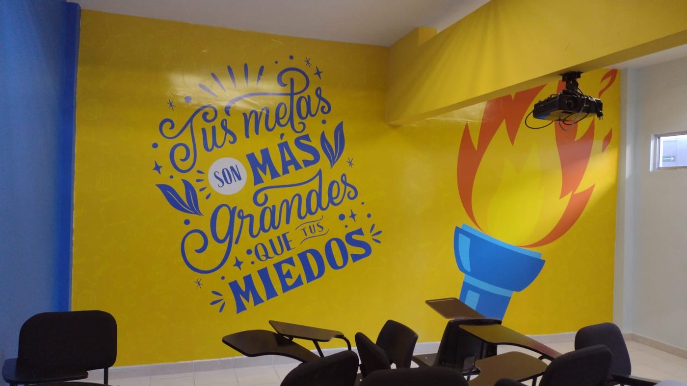 Variante en color amarillo del mural escolar motivacional 'Tus metas son más grandes que tus miedos' con tipografía caligráfica azul y antorcha encendida ilustrada, instalado por Punto Clave en aula educativa