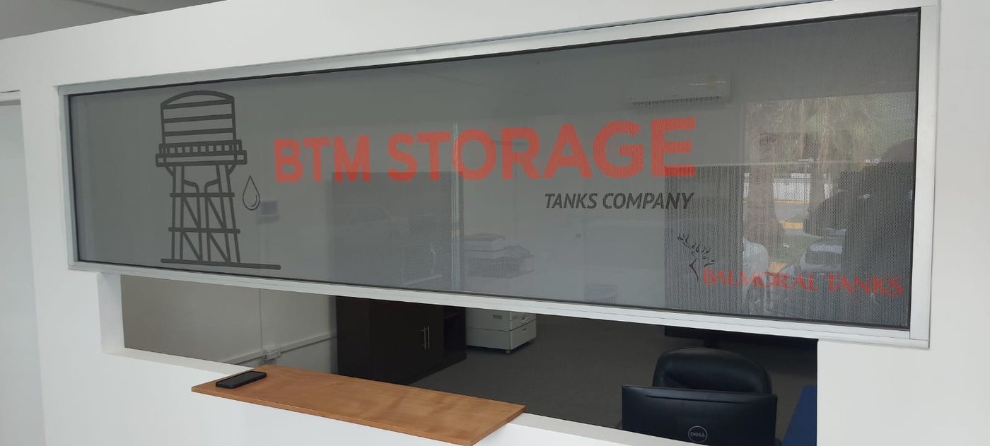 Ventana de recepción de oficinas BTM Storage Tanks Company con vinil esmerilado microperforado mostrando logotipos BTM y Balmoral Tanks e ilustración de tanque de agua, instalado por Punto Clave