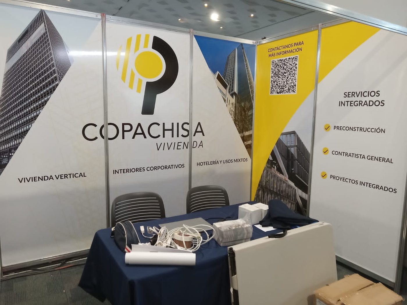 Stand de exhibición de Copachisa Vivienda en feria de construcción con paneles de vinil impreso mostrando logotipo, servicios integrados y proyectos arquitectónicos, instalado por Punto Clave
