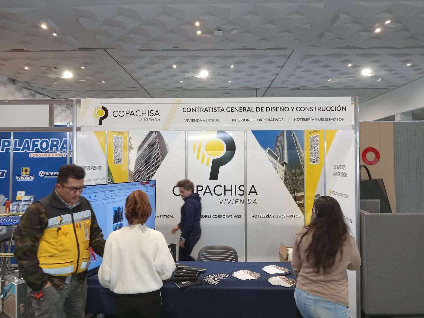 Vista panorámica del stand de Copachisa Vivienda en feria de construcción con banda superior 'Contratista General de Diseño y Construcción' y paneles fotográficos instalado por Punto Clave